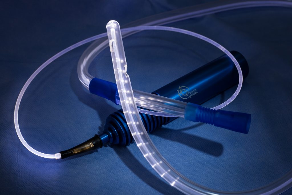 the blue handle of the device with long light fiber illuminated, end of the tube is curved, with small hole openings on both sides.